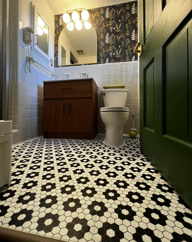 Bathroom with patterned tile floor, woody  vanity, partition  mirror, and decorative wallpaper, viewed from a debased  space  adjacent   the doorway