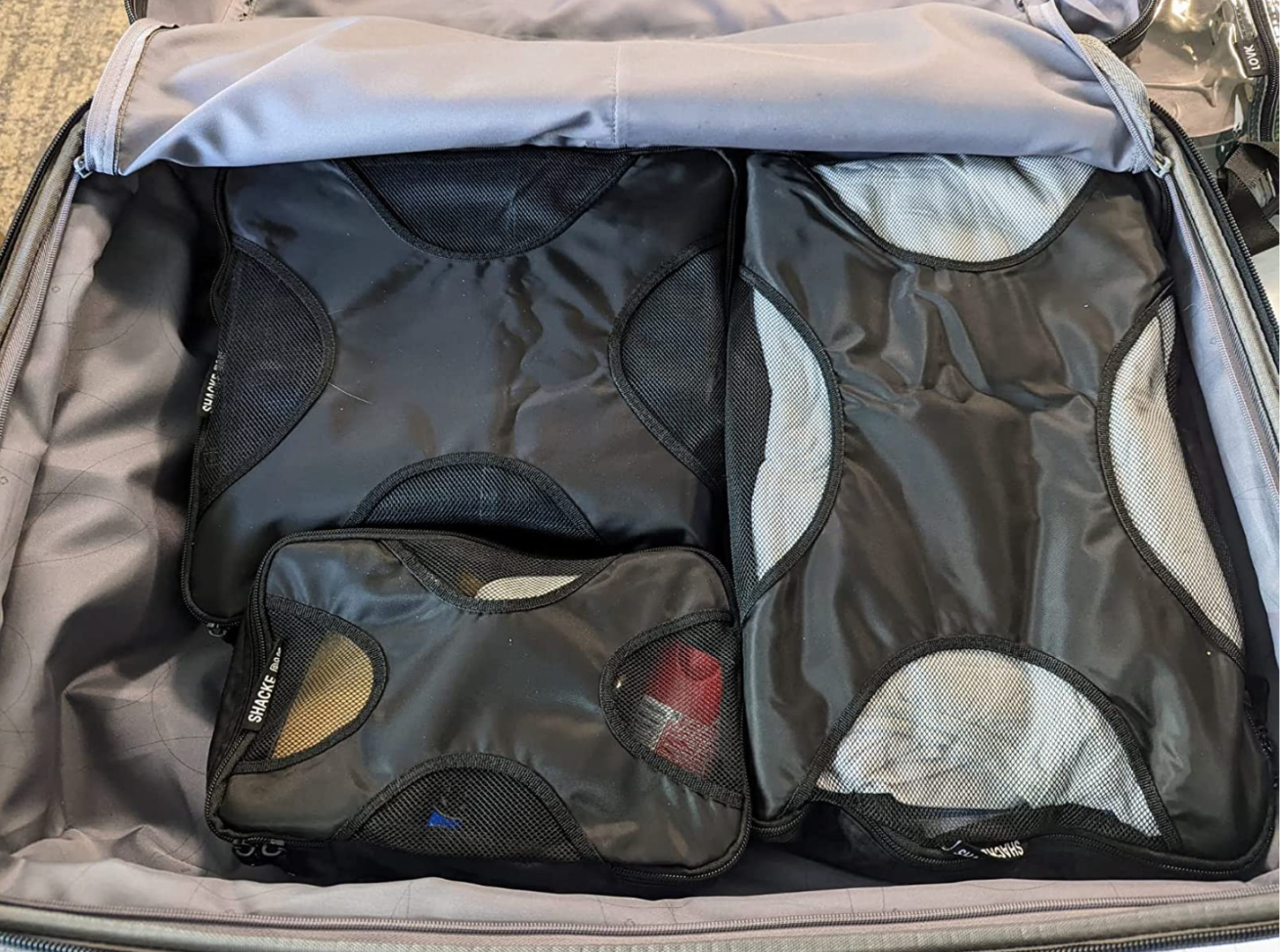 A suitcase divided with clothes in three differently-sized mesh black packing cubes 