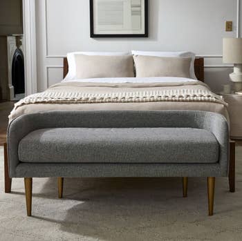 gray upholstered bench with back support at the foot of bed