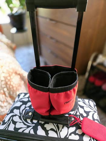 Red travel bag with black handles on a patterned suitcase, featuring a pink luggage tag
