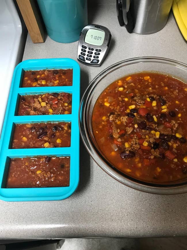 A vessel of chili with beans and maize adjacent to a freezer tray filled with portions, acceptable connected a room antagonistic adjacent a integer timer