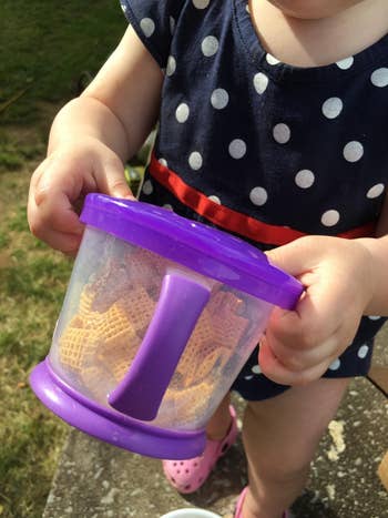 reviewer's child holding purple snack catcher with snacks in it