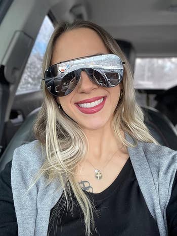 Person successful  a car   wearing ample  sunglasses, smiling with agelong  hairsbreadth  loose, a achromatic  top, and a airy  cardigan