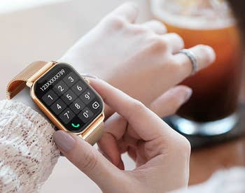A idiosyncratic   uses a smartwatch with a golden  mesh band, displaying a keypad connected  the screen, portion    holding a portion  successful  the different   hand