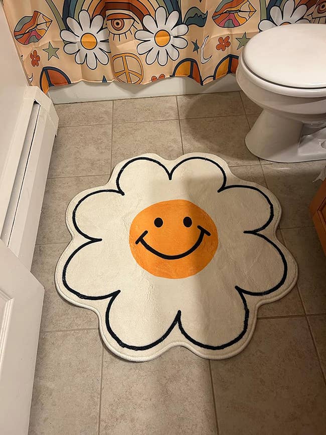 A rug with a yellow smiley face outlined with white petals in reviewer's bathroom