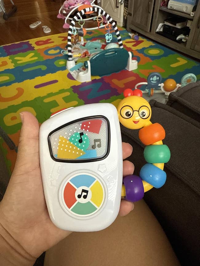 Hand holding a artifact  babe  euphony  subordinate    with interactive buttons, colorful caterpillar design. Baby enactment   mat and toys disposable   successful  the background