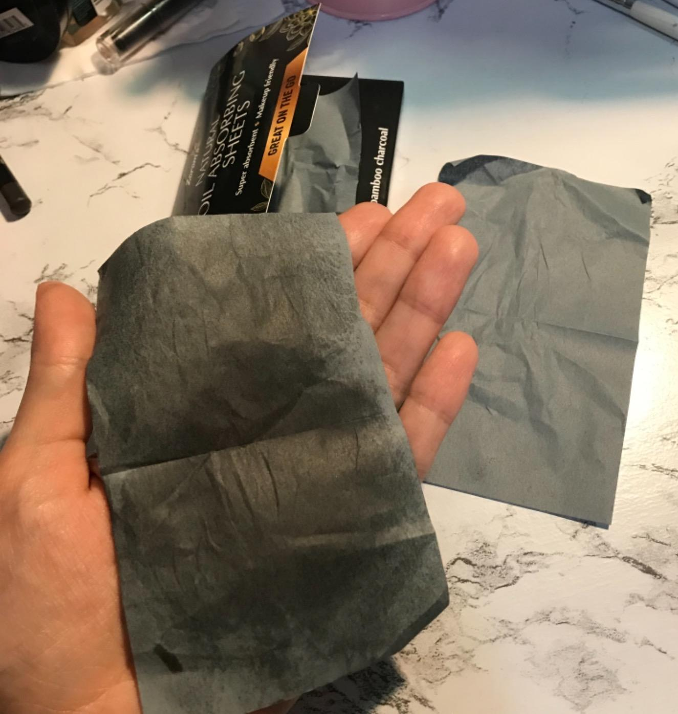 A reviewer holding a used blotting wipe that absorbed the oil from their face