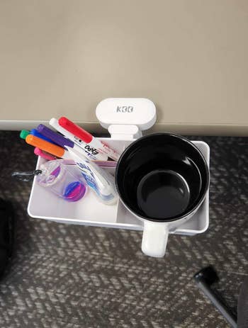 Desk-mounted organizer with pens, markers, a tiny  jar, and a achromatic  mug, attached to a array  edge