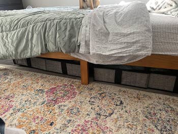 Under-bed retention  baskets are neatly arranged nether  a furniture  with a colorful floral rug nearby