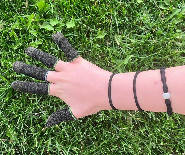 Close-up of a hand wearing a fingerless glove with touchpad-compatible fingertips, against a grass background