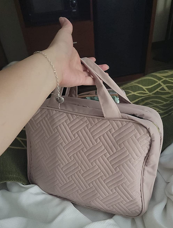 reviewer holding the pink toiletry bag, which is folded up into a small carrying case