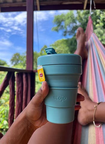 reviewer in a hammock holding teal collapsible coffee cup