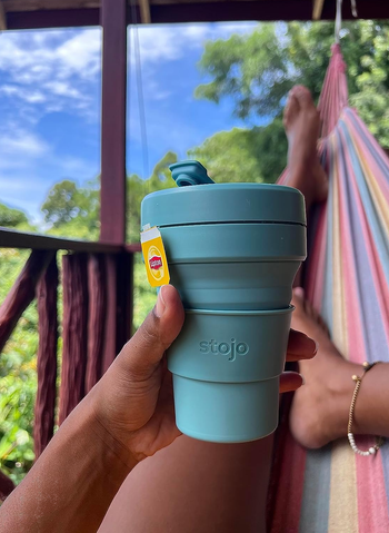 reviewer in a hammock holding teal collapsible coffee cup