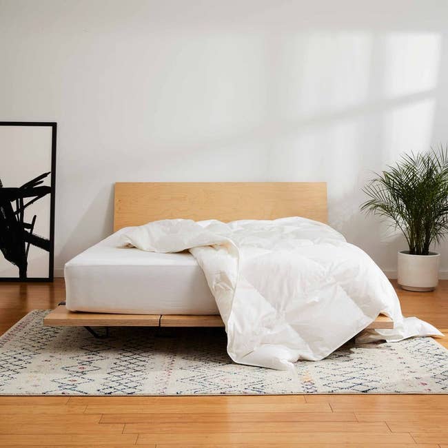 Modern wooden bed frame with white comforter on it