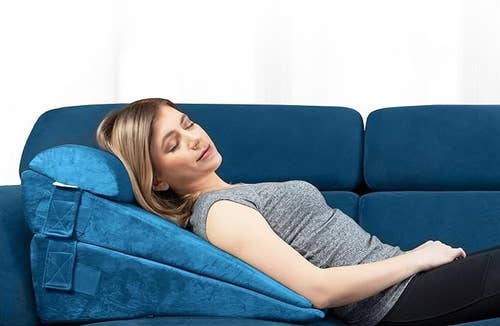 model lying down on couch using three of the blue wedge pillows