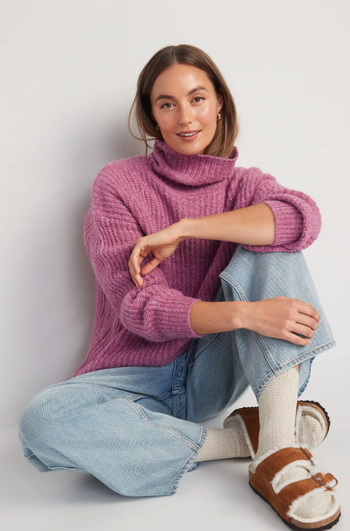 a model in a pink turtleneck sweater with the neck part up