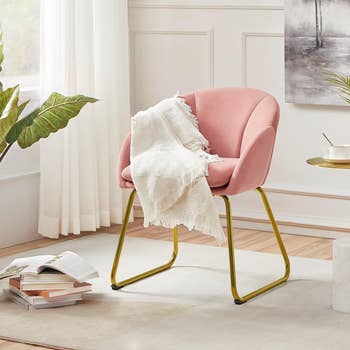 pink velvet chair with gold legs and a white throw blanket