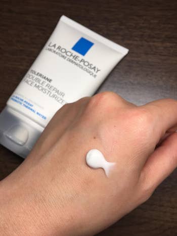 reviewer photo of swatch of moisturizer on the back of hand, with tube in the background