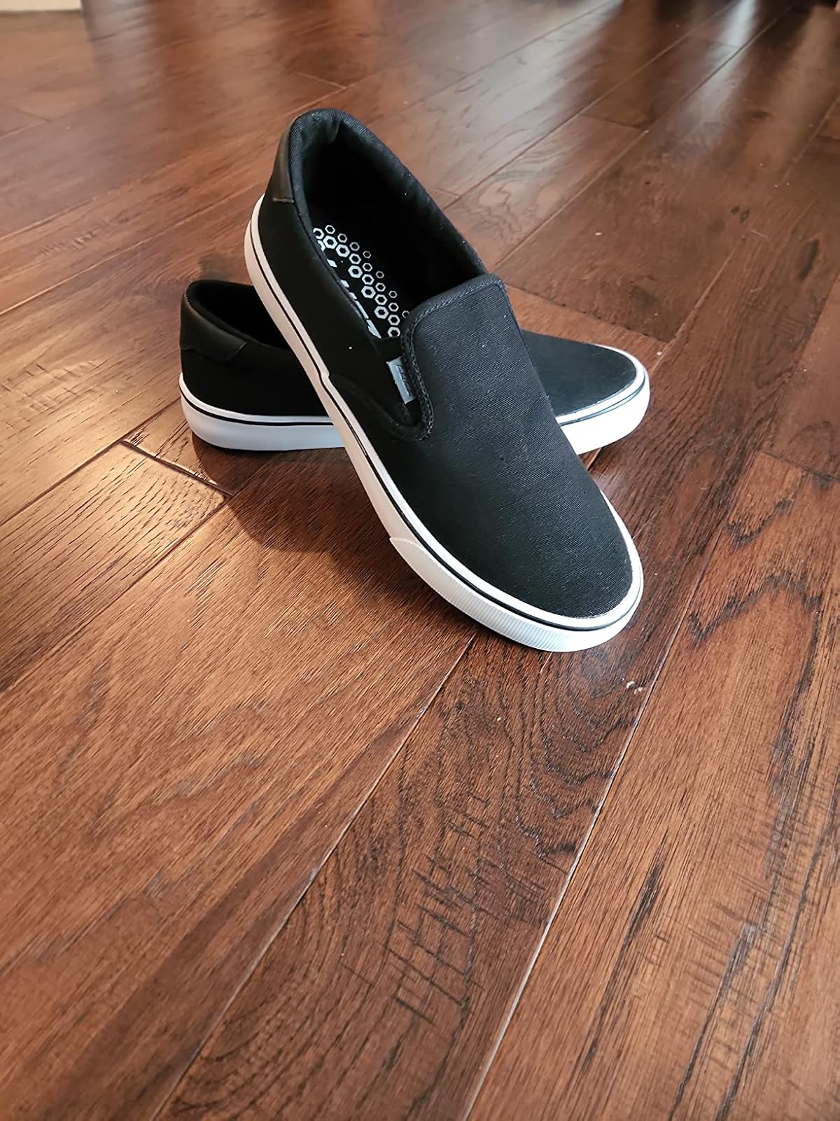 Black slip-on shoes with achromatic  soles placed connected  a woody  floor. Casual, versatile plan  suitable for mundane  wear