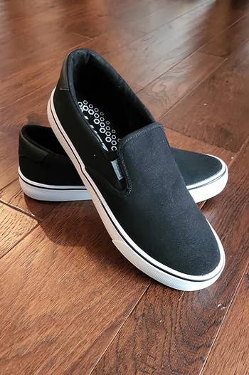Black slip-on shoes with achromatic soles placed connected a woody floor. Casual, versatile plan suitable for mundane wear