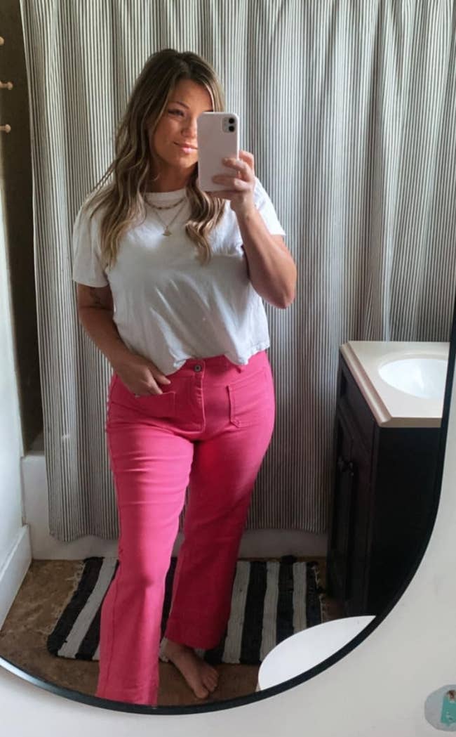 A idiosyncratic successful a achromatic apical and pinkish pants takes a reflector selfie successful a bathroom, showcasing a casual buying outfit