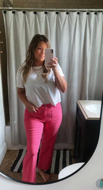 A idiosyncratic successful a achromatic apical and pinkish pants takes a reflector selfie successful a bathroom, showcasing a casual buying outfit