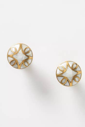 Pair of round metal earrings with intricate cut-out designs and central gemstone, on a white surface