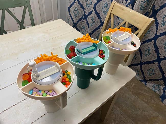 Three plastic snack trays on a table, each filled with cheese curls, candies, and gum balls, suitable for convenient tabletop snacking solutions