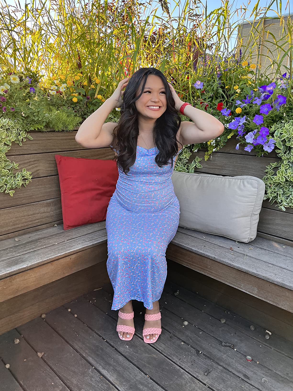 Woman successful  a floral formal  sitting connected  a woody  seat  surrounded by flowers, smiling and holding her hair