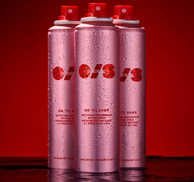 Three cans of pinkish  O/S mounting  spray with h2o  droplets connected  a reddish  background, utilized  for long-lasting constitution  application