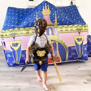 child in knight's costume in front of castle themed blow up fort