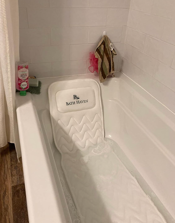 A white mat laid across a bathtub with a propped up pillow 