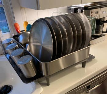 Stainless steel dish rack with plates and cups on a kitchen counter next to a sink