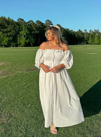 Reviewer in white off-shoulder maxi dress and sandals standing in a field