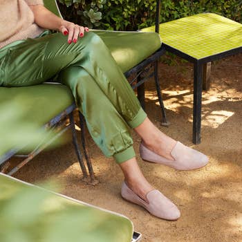 Model sitting wearing green pants and the same shoes but in latte
