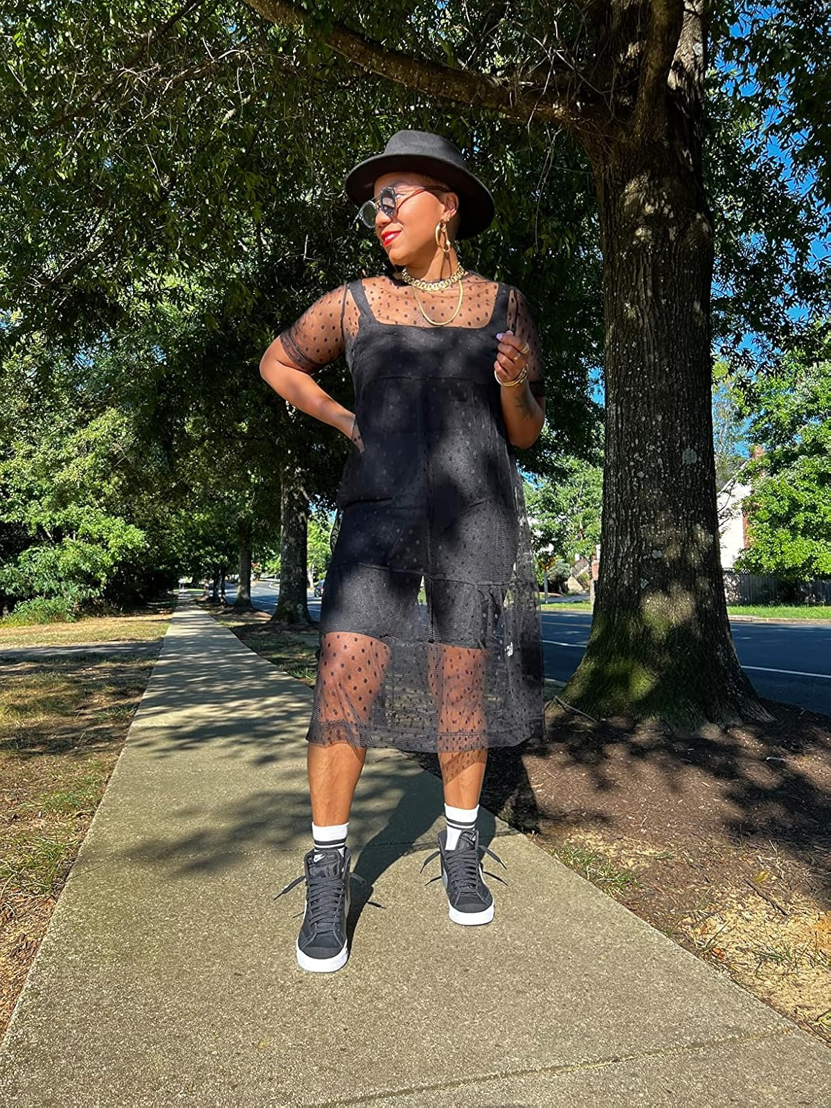Person wearing a sheer achromatic  formal  implicit    shorts, layered necklaces, and sneakers, lasting  connected  a sidewalk. They are besides  wearing a chapeau  and sunglasses
