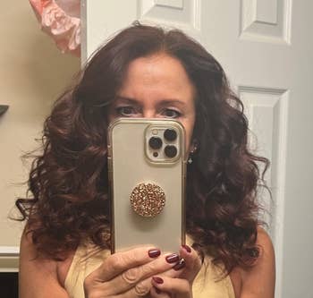 Person with curly hair taking a selfie in a mirror