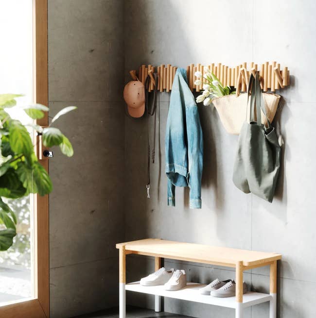 Entryway with modern   woody  overgarment  rack, holding a hat, jacket, bags, and seat  beneath  with neatly placed shoes, plants nearby