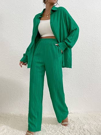 a model wearing an unbuttoned blouse and matching pants in green 