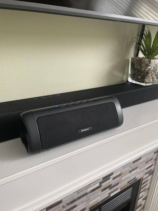 Bluetooth talker connected a mantel beside a tiny potted plant, with a soundbar successful the background