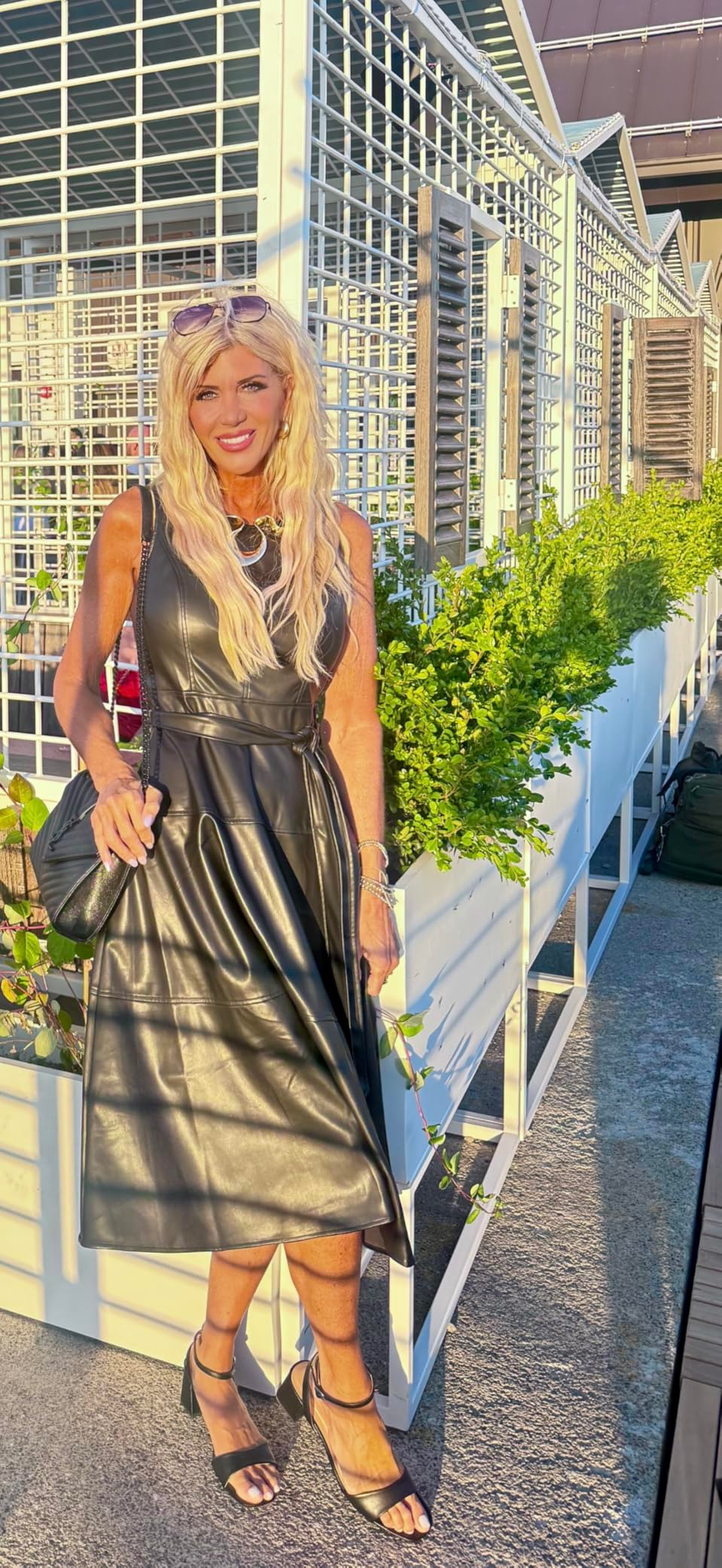 Person successful  a sleeveless leather dress, holding a achromatic  bag, stands beside planters connected  an outdoor terrace