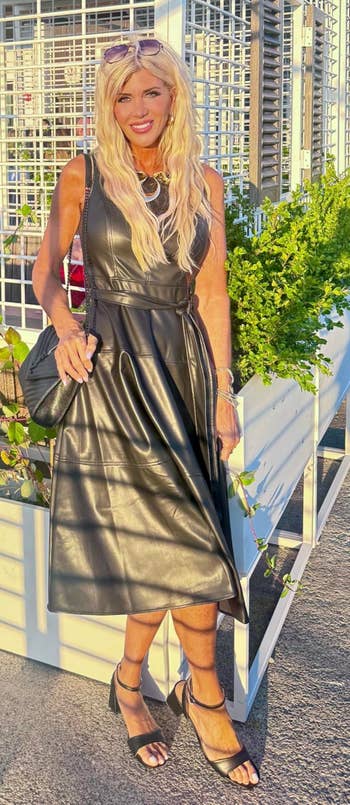 Person successful a sleeveless leather dress, holding a achromatic bag, stands beside planters connected an outdoor terrace