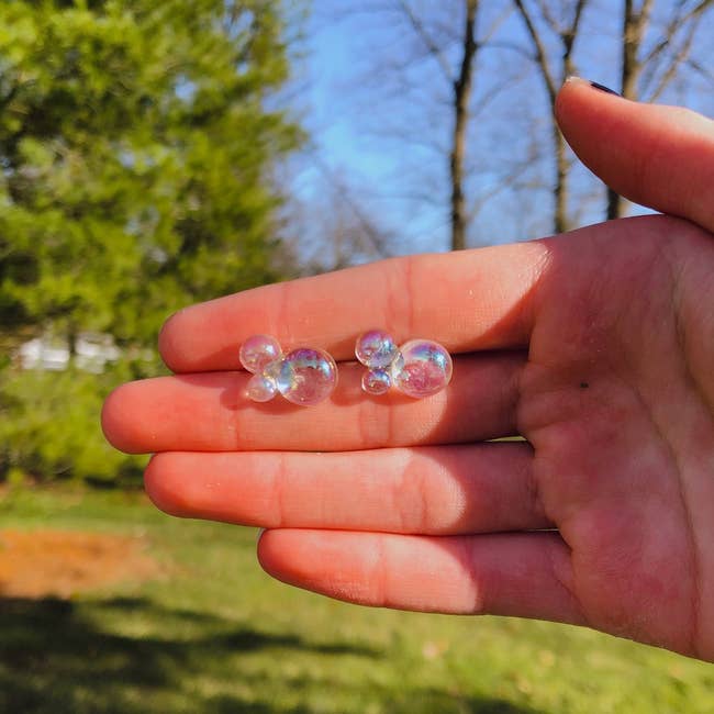 A manus holding 2 small, wide bubble clusters outdoors, with trees and writer successful the background