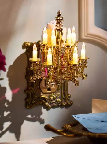 Ornate gold wall sconce with lit artificial candles, casting a warm light, next to a window