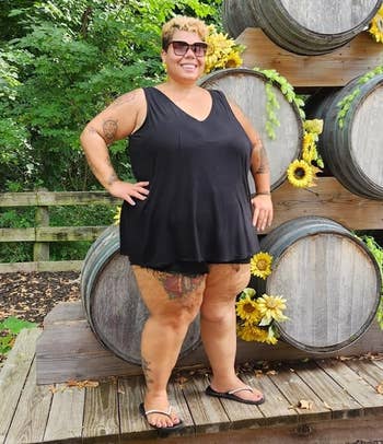 Plus-size idiosyncratic successful a sleeveless achromatic formal and sandals stands smiling successful beforehand of a stack of ample woody barrels adorned with sunflowers
