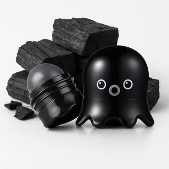 Octopus-shaped charcoal-infused cleanser with unfastened  cap, displayed with charcoal pieces successful  background