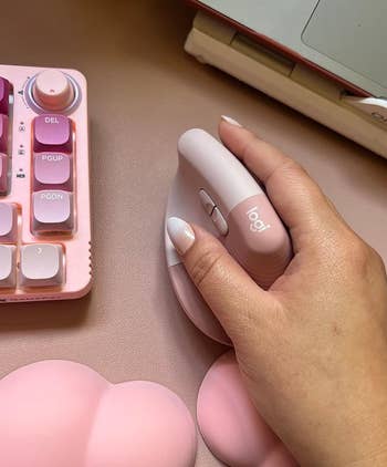 Person's hand using a Logitech computer mouse next to a pink keyboard