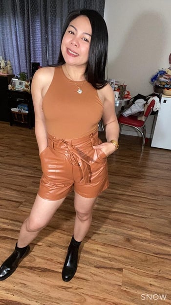another reviewer wearing the tan bodysuit with faux leather tan shorts and black boots