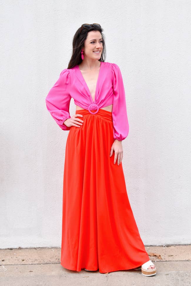 model in long sleeve gown with pink v neck bodice with waist cutouts and buckle and red skirt