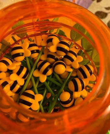 A jar filled with bee-themed toys with yellow and black stripes, arranged on green stems